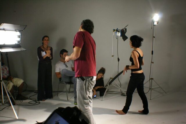 Foto com Maria Paula Fernandes (CEO Gota), Marcos Prado (diretor), Letícia Sabatella (atriz) e produção nos bastidores da campanha "É a Gota D'água +10". Equipe aparece conversando durante possível pausa entre gravações. Estão em estúdio branco,